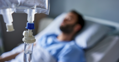 A man lies in a hospital bed receiving an IV drip.